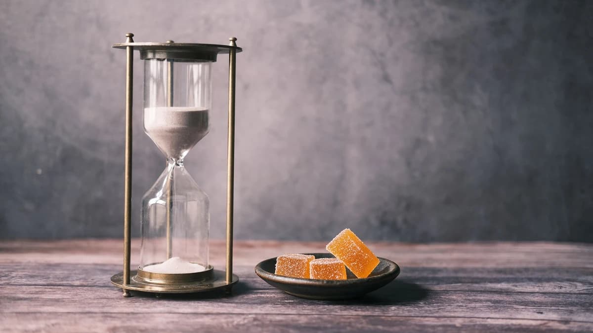 A small dish of Delta-9 gummies beside a brass hourglass on a wooden table