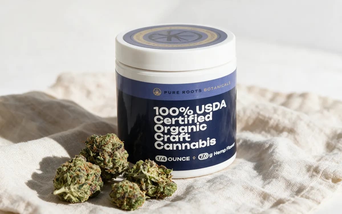 Jar of Pure Roots USDA Certified Organic THCA flower with loose buds on cream linen