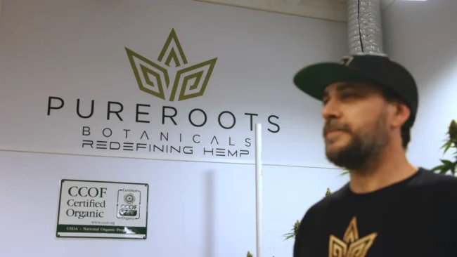 USDA Certified Organic and CCOF signage on the wall of Pure Roots Botanicals hemp farm with owner in foreground